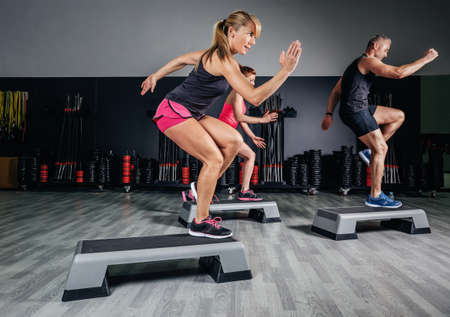 Athletic woman trainer doing aerobic class with steppers to people group on a fitness center. Sport and health concept.