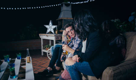 Portrait of handsome young man sitting and talking with a female friend holding beer in a outdoors party. Friendship and celebrations concept.の写真素材