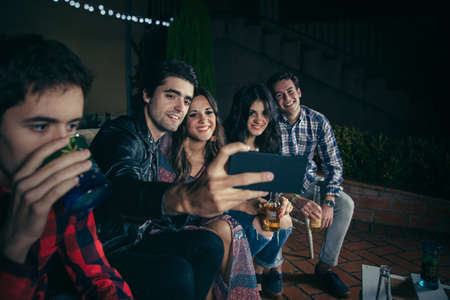 Group of happy young friends drinking and taking a selfie photo with smartphone in a outdoors party. Friendship and celebrations concept.の写真素材