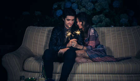 Portrait of happy young couple in love smiling and holding sparklers in a outdoors party. Love and celebrations concept.の写真素材