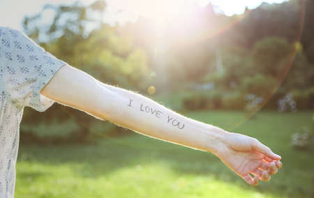 Closeup of male arm with the text -I love you- written in the skin over a sunny nature backgroundの写真素材