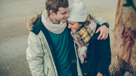 Portrait of young couple in love with hat and scarf embracing and laughing in a cold autumn day....