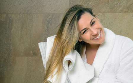Portrait of beautiful young woman with bathrobe wiping her wet hair with a towel after the shower. Health and beauty concept.の写真素材