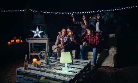 Group of happy young friends holding sparklers and having fun in a outdoors party. Friendship and celebrations concept.の写真素材