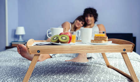 Healthy breakfast served on a wooden tray ready to eat and a happy couple in love hugging in the...