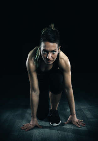 Portrait of beautiful athletic woman posing ready to run over dark backgroundの写真素材