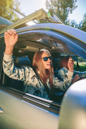 Portrait of happy young woman raising her arms and having fun inside of car in a road trip adventure. Female friendship and leisure time concept.の写真素材