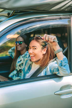 Portrait of happy young woman showing keys of new car with her friend ready to start a travel....