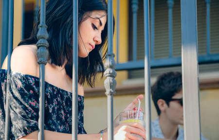 Portrait of young thoughtful woman with a lemonade glass in her hands sitting outdoors on the home stairs. Young people problems concept.の写真素材