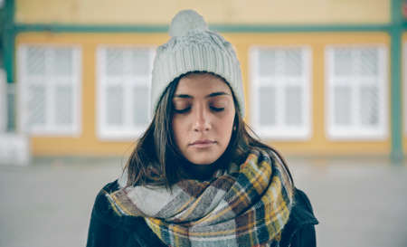 Portrait of young beautiful girl with closed eyes wearing hat and scarf in an autumn rainy day