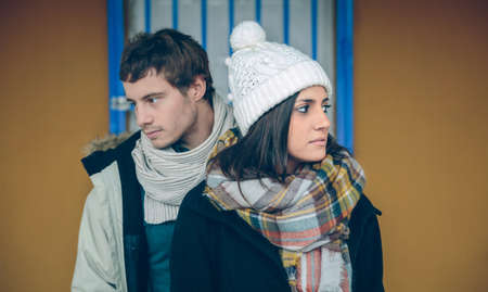 Close up of young couple wearing winter clothes standing and looking sideways outdoors. Focus on...