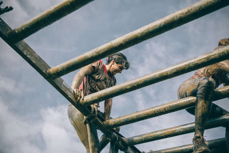 GIJON, SPAIN - JANUARY 31, 2016: Runners into the Farinato Race, a extreme obstacle race, celebrated in Gijon, Spain, on January 31, 2016. Dirty woman climbing metallic structure in test of the race.のeditorial素材