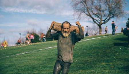 Gijon, Spain - January 31, 2016: Runner into the Farinato Race, a extreme obstacle race, celebrated in Gijon, Spain, on January 31, 2016. Strong senior man carrying wooden logs in a test of the race.のeditorial素材