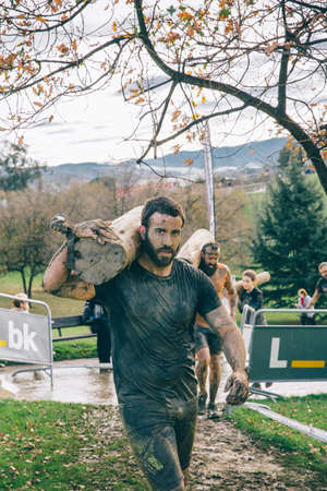 Gijon, Spain - January 31, 2016: Runners into the Farinato Race, a extreme obstacle race, celebrated in Gijon, Spain, on January 31, 2016. Dirty man carrying wooden logs in a test of the race.のeditorial素材