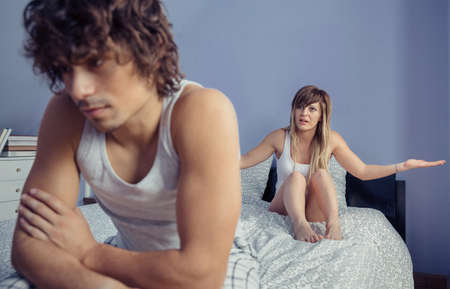 Young woman sitting over bed raising her arms and having argument to angry man in a quarrel. Couple relationship and problems concept.の写真素材