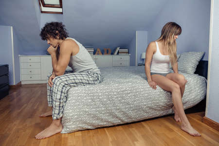 Portrait of angry young couple sitting over bed back to back after a hard quarrel. Couple relationship and problems concept.の写真素材