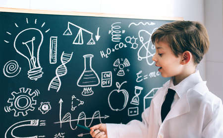 Little boy scientist showing mathematical drawing on blackboard with markerの写真素材