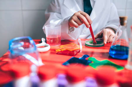 Close up of little boy hands playing with colorful liquids over red tableの写真素材