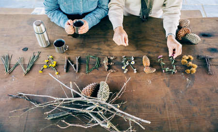 Senior couple holding coffee cups and making wanderlust word with natural objects over wooden table