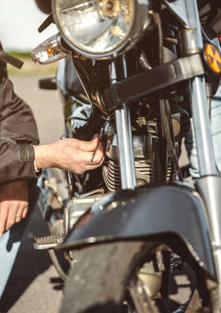 Close up of senior man repairing damaged motorcycle engine on the roadの写真素材