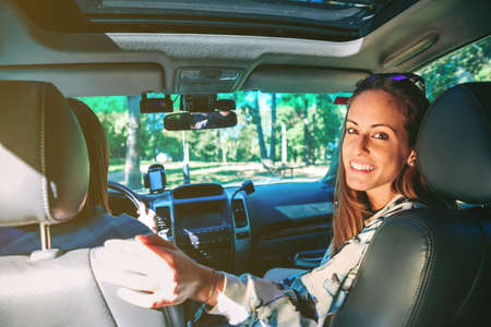 Portrait of happy young woman smiling sitting inside of car while her friend driving in a road trip...