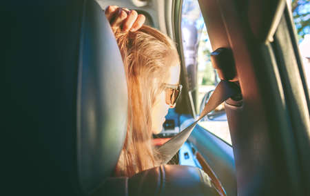 Back view of beautiful young woman with sunglasses looking the landscape through the window car during a travelの写真素材