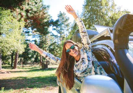 Portrait of happy young woman raising her arms through the window car in a sunny day over a nature background.の写真素材