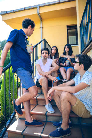 Group of young people talking and enjoying leisure time outdoors sitting on the home stairs steps. Young people lifestyle concept.の写真素材