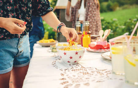 Close up of unrecognizable young woman taking chips potatoes from bowl in a outdoors summer barbecueの写真素材
