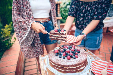 Closeup of unrecognizable woman serving naked chocolate cake with cream and berries in a outdoors summer partyの写真素材