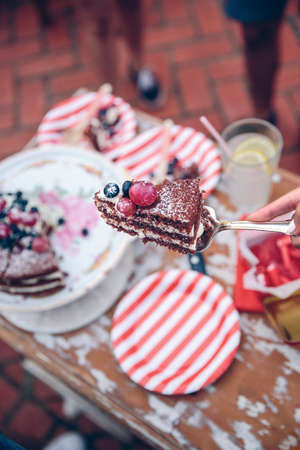 Close up of woman hand holding piece of naked chocolate cake with cream and berries in a server