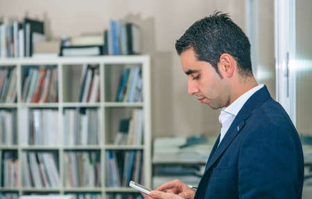 Close up of handsome businessman looking smartphone over office background
