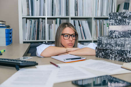 Close up of exhausted blonde secretary looking at folders stack waiting to archive in her desktop