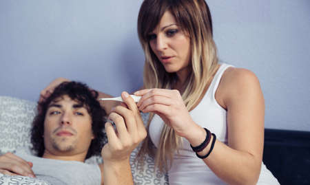 Portrait of young woman looking temperature of sick man in thermometer. Sickness and healthcare concept.の写真素材
