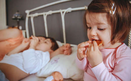 Closeup of happy little girl eating cookies in the bed with her family in a relaxed morning. Weekend...