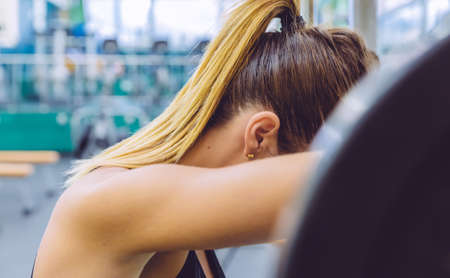Beautiful sporty woman resting tired after lifting barbell on a muscular training in fitness centerの写真素材