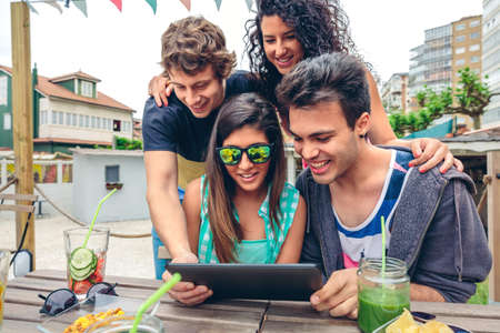 Young happy people looking electronic tablet sitting around of table with healthy drinks in a summer day outdoors. Young people lifestyle concept.の写真素材
