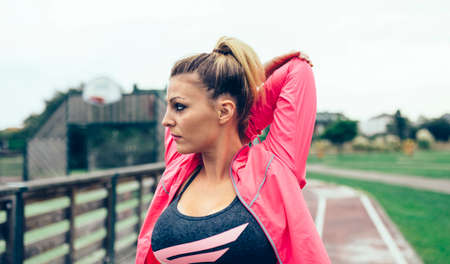 Portrait of young blonde woman with pigtail stretching arms before training outdoors