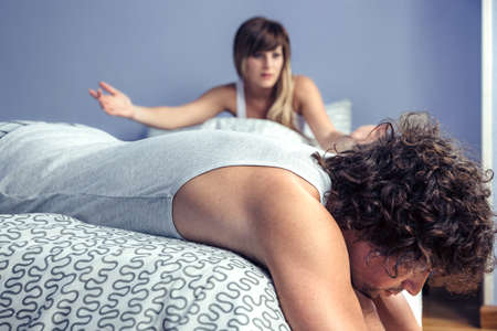 Thoughtful man lying over bed and listening to angry woman having argument in a quarrel. Couple relationship and problems concept.の写真素材