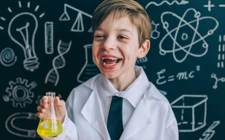 Portrait of happy little scientist laughing while holding flask with yellow liquid insideの写真素材