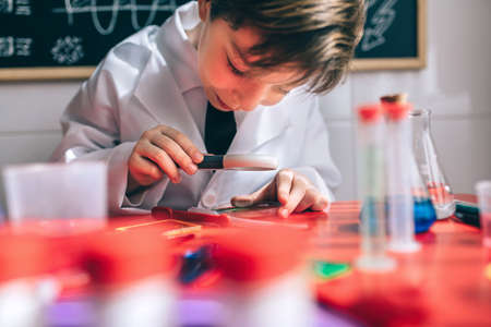 Close up of happy little scientist looking chemical liquid with magnifier against of drawn blackboardの写真素材