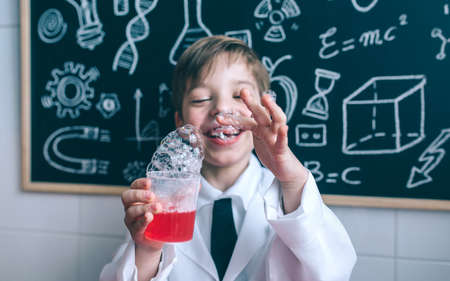 Portrait of happy little boy holding glass with soap foam against of blackboard with drawingsの写真素材