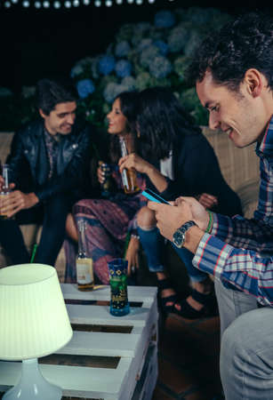 Portrait of happy man looking his smartphone in a outdoors party with friends. Friendship and...