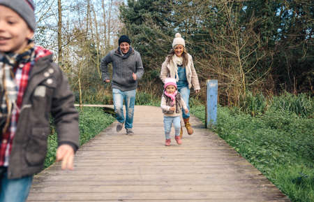 Happy family running and having fun together over a wooden pathway into the forestの写真素材