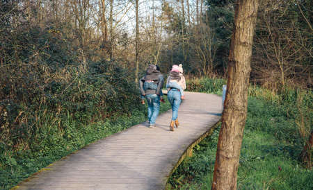 Back view of parents giving piggyback ride to children while running over a wooden pathway into the forestの写真素材