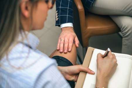 Closeup of boss putting hand over legs of blonde secretary in the office. Sexual harassment at work concept.の写真素材