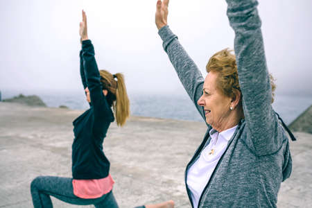 Senior woman stretching with female coach by sea pier
