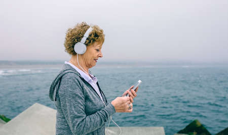 Senior sportswoman with headphones using her smartphone by sea pierの写真素材