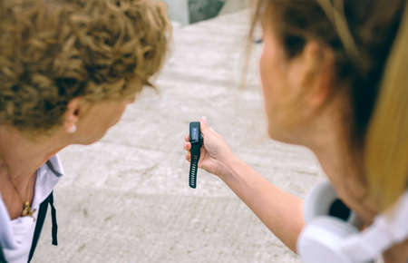 Senior woman looking smart watch with female coach outdoorsの写真素材