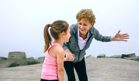 Senior sportswoman talking to little girl by pier seaの写真素材
